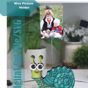 May include: A decorative wire picture holder with a snail design in green and teal. The snail holds a photograph of a woman and child. The text "Digital Cut File/SVG" is visible. The holder is a charming home decor item.