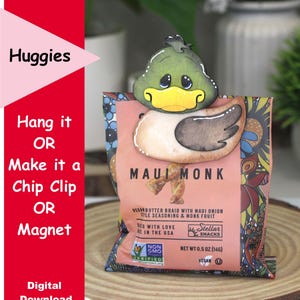 May include: A wooden duck-shaped chip clip holding a bag of Maui Monk vegan snacks. The duck has a green head, yellow beak, and brown wing. Text on the bag reads "Maui Monk" and "Vegan Butter Braid". The image also includes the text "Huggies" and "Digital Download".