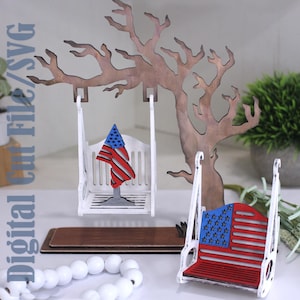 May include: A laser-cut wooden display featuring a brown tree silhouette, a white swing with a small American flag cutout, and a separate white swing with a red and blue American flag pattern. The text Digital Cut File/SVG is visible on the left.