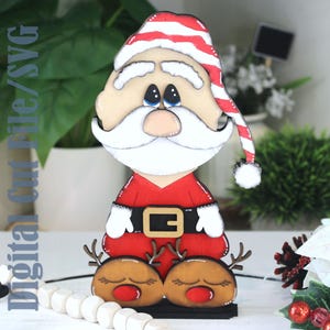 Op de afbeelding: Een houten kerstmanfiguur met een rood pak, witte baard en gestreepte hoed. De figuur heeft rendierpoten en een zwarte basis. De tekst "Digital Cut File/SVG" staat aan de linkerkant. Een feestelijke vakantiedecoratie.