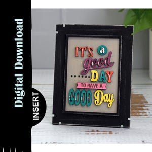 May include: A framed sign with the text "It's a good...day to have a good day" in colorful letters. The frame is black with a distressed finish.