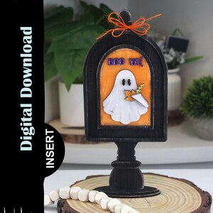 May include: A black wooden Halloween decoration shaped like a mailbox, featuring a white ghost holding a leaf and the words "BOO YA!". The decoration is adorned with an orange bow and sits on a wooden base.