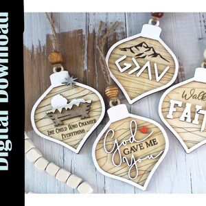 May include: Wooden Christmas ornaments with religious themes. Each ornament has a unique design and text, including a nativity scene, mountain scene, and phrases like "God Gave Me You" and "Walk by Faith."