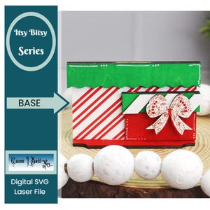 May include: A wooden base for a Christmas gift box craft project. The base is red and white striped with a green top and a red bow.