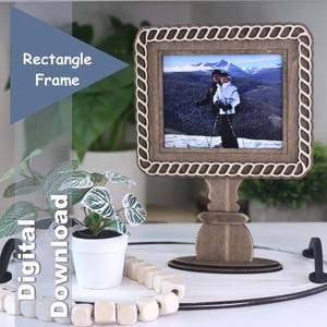 May include: A wooden rectangle frame with a decorative rope-like border, displaying a photo of people skiing in the mountains. The frame is mounted on a stand. The text "Rectangle Frame" and "Digital Download" are visible.