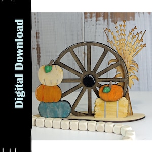 May include: A wooden fall-themed decoration featuring a stacked pumpkin design in cream, orange, and blue, a wooden wagon wheel, and a bundle of wheat. The decoration includes a small orange pumpkin on a hay bale. The text "Digital Download" is on the left.