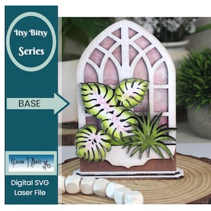 Peut inclure: Une base en bois découpée au laser avec un motif de fenêtre, comprenant des feuilles tropicales vertes et roses et une petite plante. La base porte le texte "Itsy Bitsy Series" et "Digital SVG Laser File". Le design est posé sur une tranche de bois.