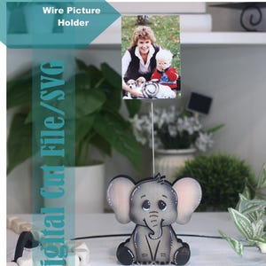 May include: A wire picture holder featuring a gray elephant figurine with large ears and a smiling face. The holder displays a photograph of a woman and child. Text on the image reads "Wire Picture Holder" and "Digital Cut File/SVG".