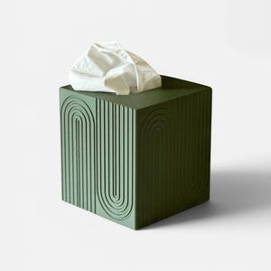 May include: A square, olive green tissue box cover featuring a textured, repeating arch pattern on its exterior surfaces. A single white tissue protrudes from the top opening of the box, which is designed to hold standard square tissue boxes.