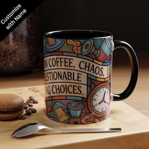 Op de afbeelding: Een koffiemok met zwarte handgreep met de tekst "ON COFFEE, CHAOS, QUESTIONABLE, MAKING CHOICES." De mok heeft een kleurrijk cartoon-ontwerp met een klok, een koffiekopje en andere illustraties. Een lepel en een macaron staan op de voorgrond.