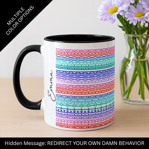 May include: White ceramic mug with a black handle and interior. The mug features a colorful geometric pattern in shades of red, pink, blue, and purple. The name "Emma" is written on the side. Text on the mug reads "Hidden Message: REDIRECT YOUR OWN DAMN BEHAVIOR."