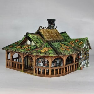 Könnte beinhalten: Ein Miniatur-Holzhaus mit einem Strohdach und einem grünen, beblätterten Dach. Das Haus hat eine Veranda mit Holzgeländern und Steinmauern.