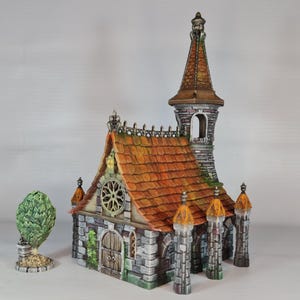 May include: A miniature stone church with a pointed roof, a bell tower, and a small, green bush in front. The church has a brown tiled roof and a stone facade with arched windows and a door.