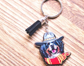 Peut inclure: Un porte-clés fantaisie avec un chien souriant portant un chapeau de cowboy et une écharpe rouge à rayures jaunes. Le chien a des poils noirs, bruns et blancs. Le porte-clés a un anneau argenté et un pompon noir.