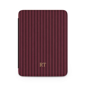 May include: A burgundy and dark burgundy striped case with the gold letters "RT" on the front. The case has a rectangular shape with rounded corners. The case is likely for a tablet or e-reader.