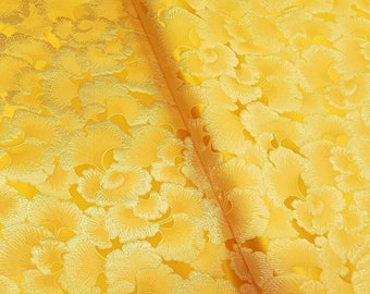 May include: A close-up of a yellow fabric with a raised floral pattern. The fabric has a shiny, satin-like finish.