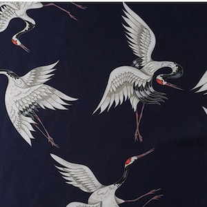 Peut inclure: Tissu bleu marine fonc&eacute; avec un motif r&eacute;p&eacute;t&eacute; de grues blanches avec des accents gris et noirs. Les grues ont des marques rouges sur la t&ecirc;te et le bec. Les oiseaux sont dans diverses poses, certains avec les ailes d&eacute;ploy&eacute;es.