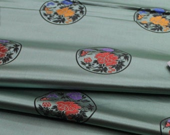 May include: Green fabric with a repeating pattern of circular designs featuring colorful flowers and leaves. The fabric is folded over itself, revealing the underside.