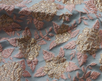 May include: A close-up of a light blue fabric with a pink and gold floral pattern. The fabric has a textured, woven look and a slightly frayed edge.