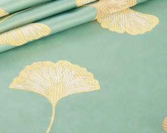 May include: A close-up of a light blue fabric with a subtle pattern of gold ginkgo leaves. The fabric is folded in thirds, showing the texture and detail of the design.