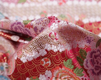 Puede incluir: Primer plano de una tela roja con un patrón floral. La tela tiene un hilo dorado tejido en el diseño, creando un efecto brillante. Las flores son rosas, blancas y verdes.