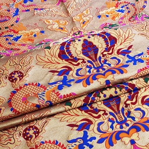 Könnte beinhalten: Goldfarbener Stoff mit einem sich wiederholenden Muster aus Drachen und floralen Designs in Rot-, Blau- und Orangetönen.
