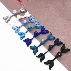 May include: A set of 10 leaf-shaped fabric closures with pearl-like beads in various shades of blue, white, and black.