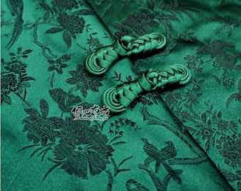 May include: Two green fabric buttons with a braided design. The buttons are on a green fabric background with a floral pattern.