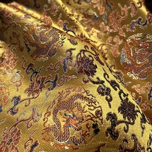 May include: Gold fabric with a repeating pattern of dragons and floral designs. The fabric has a satin-like sheen and is embroidered with blue, red, and orange thread.