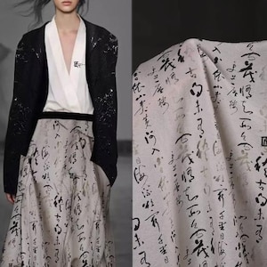 Pode incluir: Um tecido branco com escrita em estilo caligráfico preto. O tecido está drapeado sobre uma mesa e tem uma textura macia e fluida.