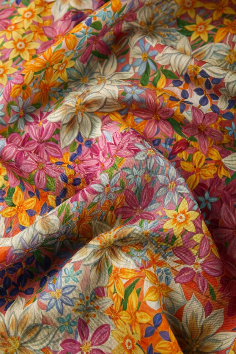 May include: A pink fabric with a floral print featuring yellow, pink, blue, and white flowers. The fabric is textured and has a soft, flowing feel.