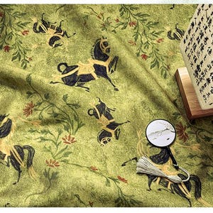 Może przedstawiać: Zielona tkanina z powtarzającym się wzorem czarnych koni ze złotymi akcentami, elementami kwiatowymi i małym dekoracyjnym wachlarzem. Widoczna jest lampa z azjatyckimi znakami.