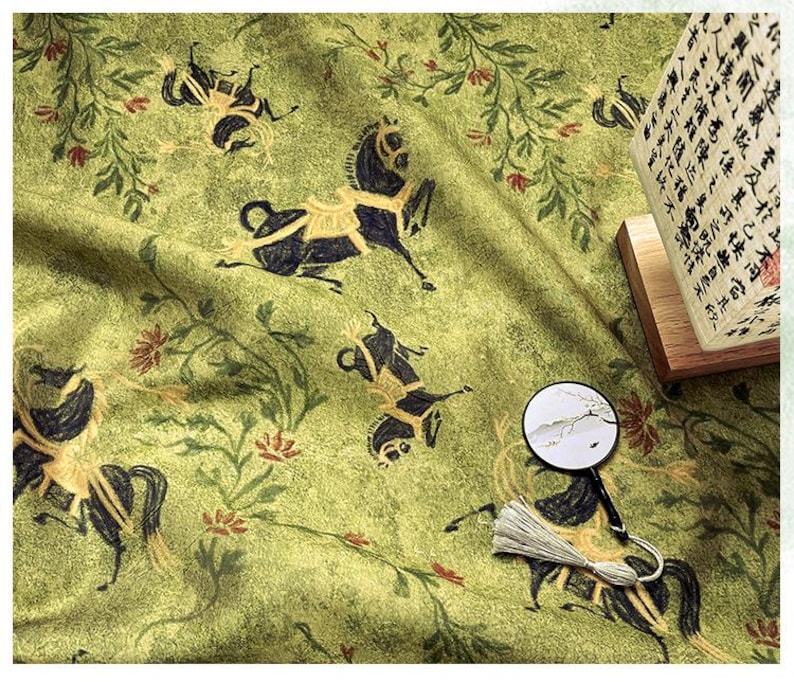 Może przedstawiać: Zielona tkanina z powtarzającym się wzorem czarnych koni ze złotymi akcentami, elementami kwiatowymi i małym dekoracyjnym wachlarzem. Widoczna jest lampa z azjatyckimi znakami.