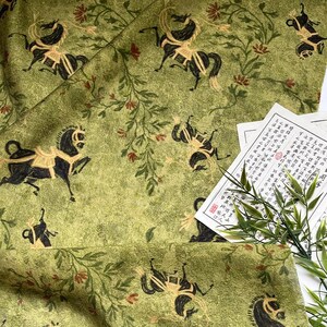 Może przedstawiać: Zielona tkanina z powtarzającym się wzorem czarnych koni ze złotymi akcentami i elementami kwiatowymi. Tkanina ma estetykę vintage, z wyblakłym wyglądem. Są też papiery z azjatyckimi znakami.