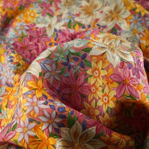 May include: A pink fabric with a floral print featuring yellow, white, and blue flowers. The fabric is folded and has a soft, textured surface.