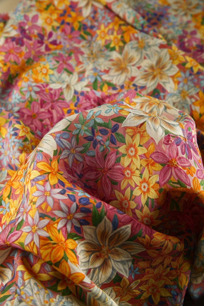 May include: A pink fabric with a floral print featuring yellow, white, and blue flowers. The fabric is folded and has a soft, textured surface.