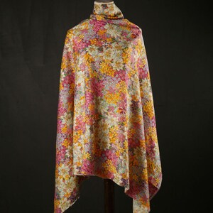 May include: A white fabric with a floral pattern in shades of pink, yellow, and orange. The fabric is draped over a mannequin.