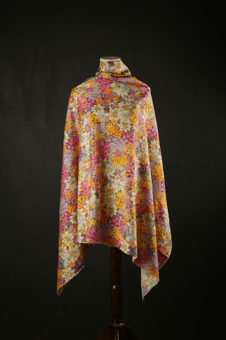 May include: A white fabric with a floral pattern in shades of pink, yellow, and orange. The fabric is draped over a mannequin.