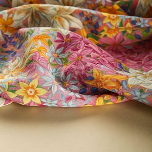 May include: A close-up of a pink and yellow floral fabric with a variety of flowers and leaves. The fabric is folded and draped over a beige surface.