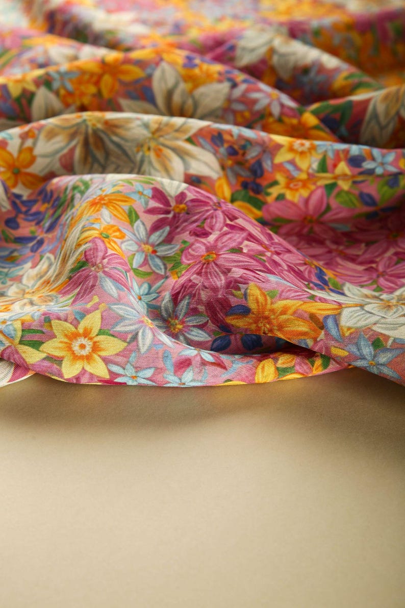 May include: A close-up of a pink and yellow floral fabric with a variety of flowers and leaves. The fabric is folded and draped over a beige surface.