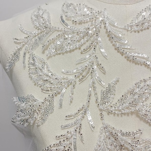 May include: White beaded lace trim with a delicate floral design. The trim features small, white beads arranged in a pattern of leaves and flowers.