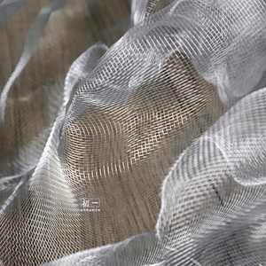 May include: Close-up of a silver mesh fabric with a soft, delicate texture. The fabric is draped and folded, creating a flowing, ethereal look.