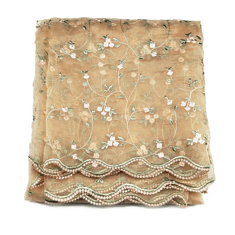 May include: A beige sheer fabric scarf with a floral embroidery pattern and a scalloped edge.