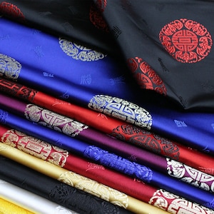 May include: A selection of patterned silk fabrics in various colours. The fabrics include shades of blue, red, gold, and black, with detailed designs and Chinese characters. The silk has a smooth, shiny texture.