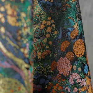 Puede incluir: Primer plano de una tela con un estampado floral detallado. El dise&ntilde;o presenta un fondo oscuro con vibrantes flores naranjas, rosas y verdes, junto con acentos dorados. La tela tiene una apariencia lujosa y texturizada.