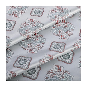 Könnte beinhalten: Nahaufnahme eines silbernen Stoffes mit einem sich wiederholenden Muster aus roten, weißen und blauen floralen Designs. Der Stoff hat einen dezenten Glanz und eine weiche Textur.
