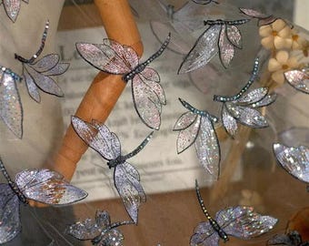 May include: A sheer fabric with iridescent dragonfly embroidery. The fabric is light and airy, perfect for creating delicate garments or accessories.