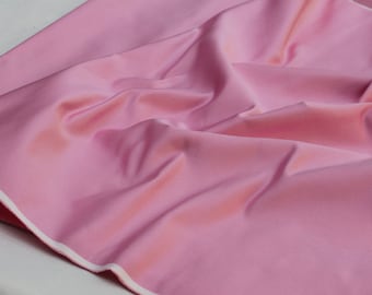 May include: A close-up of a pink fabric with a white border. The fabric is smooth and has a slight sheen.