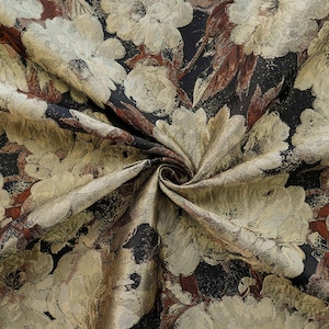 May include: A close-up of a floral fabric with a swirling pattern. The fabric features large, cream-coloured flowers with gold and brown accents against a dark background. The material has a textured appearance, suggesting a woven or embroidered design.