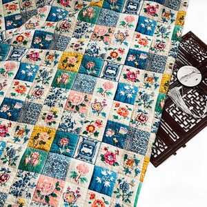 May include: A patchwork quilt with a floral design. The quilt features squares of various colors, including blue, pink, yellow, and white, each with embroidered flowers and patterns. The quilt is folded, showing its intricate design and craftsmanship.